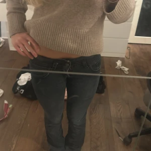 Gråa lowwaist jeans - Säljer ett par gråa jeans från Bik Bok med snygga bakfickor och guldfärgad logga. Jeansen har låg midja och utsvänga/raka. Materialet är en mix av bomull, polyester och elastan för extra komfort. KAN KLASSAS SOM SVARTA