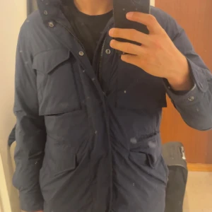Mörkblå parkajacka Polo Ralph Lauren - Parkajacka från Polo Ralph Lauren som är mörkblå med dragkedja och tryckknappar. Jackan har en klassisk badge på ärmen och är tillverkad i slitstark polyester. Perfekt för kyliga dagar och snygg till streetwear. Skriv för mer frågor och priset är diskuterbart! Ny pris ca 5200