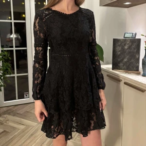 Svart spetsklänning från SHEIN XS - (klänning för liten!). Supersnygg svart kort spetsklänning från SHEIN i storlek XS. Klänningen har långärmade ärmar, volangig kjol och rygg med dragkedja. Blommigt spetsmönster och rund halsringning med små bollar som detalj. Perfekt för dig som vill sticka ut! 