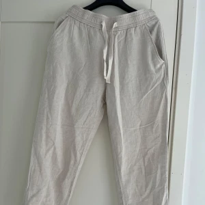 Beiga linnebyxor med snörning från Zara - Luftiga beiga linnebyxor från Zara med elastisk midja och snörning. Byxorna har sidfickor fram och passpoalfickor bak, perfekt för en chill och stilren look. Materialet är linne som ger en skön känsla, och färgen är ljusbeige. Sparsamt använda!