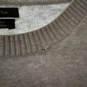 Grå stickad tröja Massimo Dutti - Grå stickad tröja från Massimo Dutti med rund halsringning och ribbade detaljer. Tillverkad i en mjuk blandning av bomull och ull som känns skön mot huden. Perfekt för lager-på-lager under kyliga dagar.