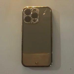 Glittrigt mobilskal med gems - Snyggt mobilskal med transparent baksida.. Kameraramen är dekorerad med glittrande stenar . Några har dock lossnat men går säkert atta limma fast nya. Skal till iPhone 13 Pro.