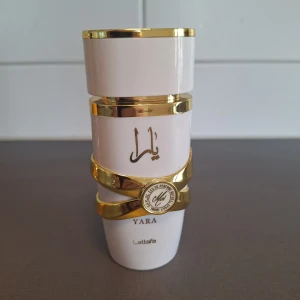 Yara Moi parfym från Lattafa - Yara Moi från Lattafa är en elegant parfym i vit flaska med guldiga detaljer och arabiska tecken. Doften har träiga, vita blommiga och pudriga toner med inslag av patchouli, karamell, amber och fruktiga noter. Flaskan har en lyxig och modern design som sticker ut. Ca 70 ml kvar