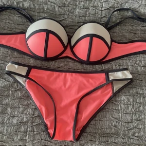 Färgstark bikini med svarta kanter - Snygg bikini i färgstark korallrosa och beige med svarta kontrastkanter. Överdelen har vadderade kupor och bygel för extra stöd, medan underdelen har en klassisk trosa med matchande färgblock. Perfekt för strandhäng och poolparty! Triangl liknande väldigt trendig och svår att få tag på! Supersnygg och cool
