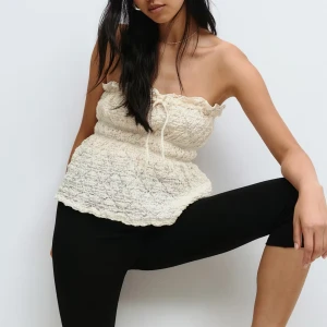 Krämvit tubtopp - Superfin krämvit bandeau tubtopp med smockad struktur och söt snörning framtill. Toppen är ärmlös och har en lätt volangkant upptill och nertill. Perfekt för varma dagar och ger en romantisk vibe till din outfit. Aldrig använd, prislappen kvar!