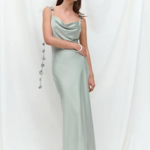 Ljusgrön långklänning med blomdetaljer - Superfin ljusgrön långklänning i satinliknande material med smala axelband och dekorativa blommor längs banden. Klänningen har en snygg draperad urringning och en elegant, slank siluett. Perfekt för dig som vill sticka ut med en unik och stilren look. Nypris 699