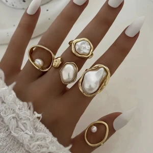 5 Guldiga ringar med pärldetaljer - Fem unika ringar i guldton med oregelbundna former och stora vita pärlor. Ringarna har en modern, konstnärlig design och ger en lyxig känsla med sina skimrande pärldetaljer. Perfekt för dig som vill sticka ut med trendiga accessoarer.