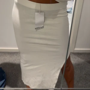 Vit långkjol  - Säljer en snygg vit långkjol från Bershka med tight passform och slits på sidan. Kjolen är enkel att matcha. Materialet känns mjukt och stretchigt, vilket gör den bekväm att bära hela dagen. Säljer då den inte kommer till användning och är lite för kort för mig