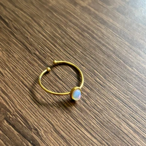 Guldfärgad ring med opalsten - Snygg guldfärgad ring med tunn, öppen design och en oval, skimrande opalsten i vitt och blått. Ringen har små detaljer runt stenen som ger en exklusiv känsla. Perfekt för dig som gillar stilrena smycken med en twist.