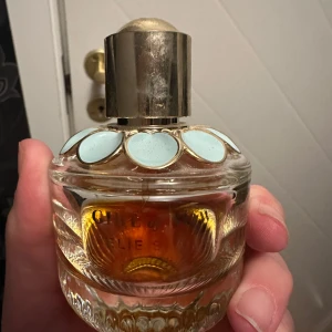 Chloé parfym Elie Saab - Säljer en lyxig parfym från Chloé Elie Saab. Flaskan är rund i tjockt glas med dekorativa ljusblå detaljer och ett stort guldfärgat lock. Parfymen har en djup bärnstensfärgad vätska och flaskan känns riktigt exklusiv och elegant.