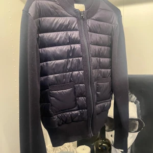 Svart quiltad cardigan jacka - Snygg svart cardigan jacka med quiltad framsida och två praktiska fickor. Jackan har ribbade muddar, dragkedja framtill och är långärmad. Perfekt för dig som gillar en stilren look med lite extra edge. Liknar Moncler jackan, använd en gång 