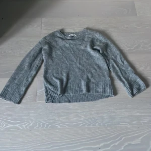 Grå stickad tröja från H&M - Mysig grå stickad tröja från H&M i storlek 134/140. Tröjan har rund halsringning, långa ärmar och bred ribbad kant nedtill och vid ärmsluten. Perfekt för kyliga dagar och enkel att matcha med jeans eller kjol.