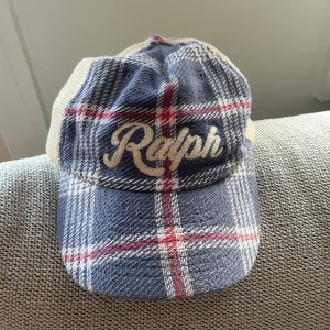 Ralph Lauren Keps - Fint rut mönster framtill och sandfärgad baktill med brunt spänne med mettal knäppe. Nypris runt 1000 kr. Använt högst 3 gånger så kanon skick. Skriv vid eventuell frågor.