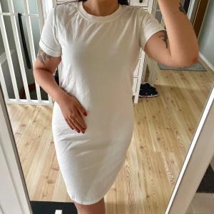 Vit t-shirtklänning från Jacqueline de Yong - Vit t-shirtklänning från Jacqueline de Yong i mjuk bomull. Modellen är lite figursydd och knälång med korta ärmar och rund halsringning. Använd endast en gång! Normal i storlek!🌸