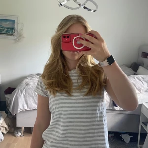 Randig t-shirt från Polo Ralph Lauren - Säljer en vit och ljusgrå randig t-shirt från Polo Ralph Lauren i storlek M. Klassisk passform med korta ärmar och rund hals. Ikoniska Polo-loggan broderad på bröstet. Tillverkad i mjuk bomull, perfekt för en chill och stilren look.