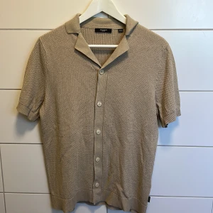 Beige stickad kofta från Jack & Jones - Snygg beige stickad kofta från Jack & Jones Premium med kort ärm och klassisk krage. Koftan har knappar hela vägen framtill och ett diskret, strukturerat mönster i materialet. Perfekt för dig som gillar en stilren och chill look.