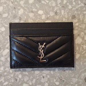 Svart YSL quiltad korthållare i skinn - Snygg svart korthållare från YSL i äkta  quiltat skinn. Korthållaren är i super bra skick, och har inga tecken av användning. 