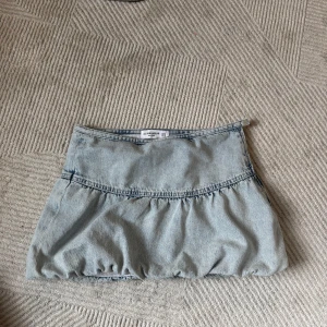 Ljusblå jeanskjol från Pull&Bear - Supersöt ljusblå jeanskjol från Pull&Bear i kort modell. Kjolen har en volangdetalj och ballongformad nederkant som ger en cool och trendig vibe. Perfekt att styla med sneakers eller boots för en chill look. Lågmidjade 