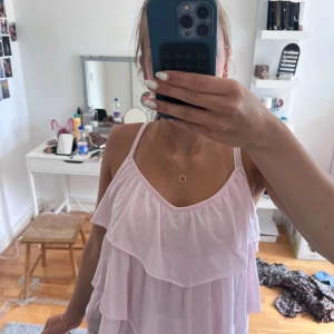 Ljusrosa volanglinne från H&M - Supersött ljusrosa linne från H&M med tunna axelband och flera lager volanger. Luftig och flowy passform, perfekt för varma dagar. Mjuk och skön bomullskänsla, passar till shorts eller kjol för en chill vibe.