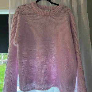 Ljusrosa stickad tröja från VILA - Superfin ljusrosa stickad tröja från VILA med grovstickad känsla och snygga flätade detaljer längs ärmarna. Tröjan har rund halsringning och långa ärmar, perfekt för att mysa i under kyliga dagar.