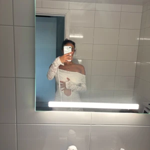 Vit spetsklänning med cut-out - Supersnygg vit kort klänning i spets med offshoulder och långärmade ärmar. Klänningen har en cut-out detalj framtill och volang nertill. Perfekt för dig som vill sticka ut med en romantisk vibe. Eller du som behöver en klänning inför studenten 