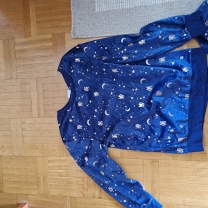 Chelsea FC pyjamasbyxor & tröja stjärnmönster - Mörkblå pyjamasbyxor & tröja från Chelsea FC med guldiga stjärnor, månar och klubbens lejonlogga. Byxorna & tröjan är i mjuk polyester och byxorna har resår i midjan för extra komfort. Perfekta för chillkvällar eller när du vill visa ditt lagstöd hemma.