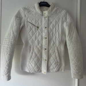 Vit quiltad jacka Holly & Whyte S - Snygg vit quiltad jacka från Holly & Whyte by Lindex i storlek S. Jackan har ribbade sidor, guldfärgade knappar och en sned bröstficka med dragkedja. Lätt figursydd passform och långärmad modell, perfekt för vår och höst. Använd sparsam.