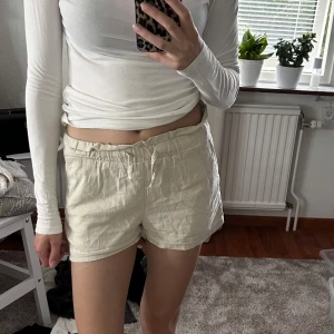 Beiga linneshorts med snörning - Snygga beiga shorts i linne med elastisk midja och snörning framtill. De har en avslappnad passform och praktiska fickor på sidorna. Perfekta för varma dagar och ger en chill vibe till din outfit.