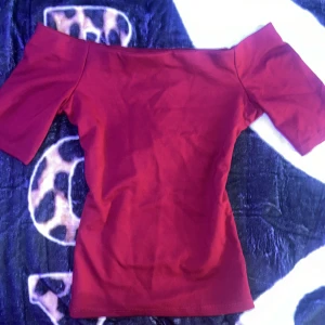 Vinröd offshoulder topp från H&M - Snygg vinröd offshoulder topp från H&M i stretchig bomullsmix. Toppen har korta ärmar och en tight passform som framhäver axlarna. Perfekt för dig som gillar en stilren och trendig look med lite edge.
