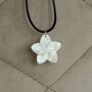 Halsband med vit blomma i pärlemor - Supersött halsband med ett hängsmycke i form av en fembladig blomma, tillverkad i skimrande vit pärlemor/snäckskal! Svart justerbart band! Perfekt för dig som gillar unika smycken till sommaren :)