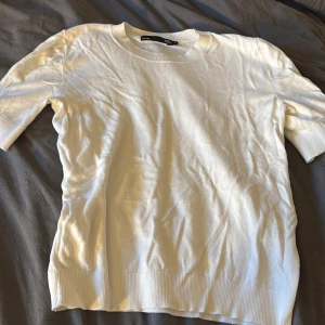 Vit kortärmad tröja från 157 - En stilren vit tröja från 157 med korta ärmar och rund hals. Tröjan har ribbade muddar vid ärmslut och nederkant, vilket ger en snygg och enkel look. Perfekt att matcha med jeans eller kjol för en clean stil.