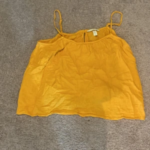 Gul croppad linnetopp med tunna axelband - Säljer en solgul croppad linnetopp med tunna axelband. Toppen har en lös passform och är perfekt för varma dagar. Enkel och stilren design som passar till många olika outfits.