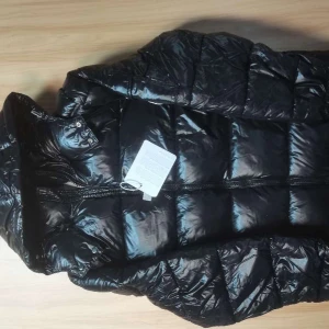 Svart dunjacka från Moncler - Säljer en svart, glansig dunjacka från Moncler med klassisk quiltad design. Jackan har lång ärm, dragkedja framtill och en ficka med Moncler-logga på ärmen. Perfekt för kyliga dagar och riktigt snygg till vintern.