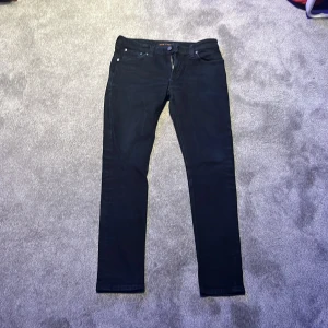 Svarta Nudie jeans  - Säljer ett par svarta jeans från Nudie Jeans Co med klassisk femficksdesign och smal passform. Byxorna har dragkedja och knapp framtill samt Nudie-logga bak på linningen. Perfekta för dig som gillar stilrena och tidlösa jeans. Har aldrig använts.