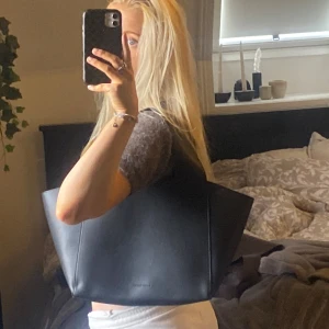 Svart carin wester läderväska  - Säljer denna snygga Carin Wester väskan! Den är köpt på Åhlens hemsida för 399kr, den heter ”Liten toteväska SANYA” på Åhlens hemsida.🌻 Den är i helt nyskick, aldrig använd. ☕️🍂😽🙌🏼🍸  Lite info: • Liten toteväska i polyuretan🍸 • Breda axelremmar😽 • Magnetknapp i toppen🙌🏼 • Fästen för fodral ur serien MIX💋  Mått på väskan: Bredd nedtill: 30 cm🦭 Bredd upptill: 50 cm🍂 Höjd: 26 cm🥀 Djup: 14 cm🌞 Dropplängd: 18 cm🪐  - väskan har invändiga remmar med fästen ☕️ 