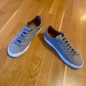 Grå sneakers med vit sula - Snygga grå sneakers med klassisk design och vit platt sula. Skorna har rund tå och snörning framtill. Perfekta för en stilren och enkel look.