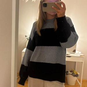 Randig stickad tröja från H&M - Mysig stickad tröja från H&M i storlek L. Tröjan har breda svarta och grå ränder, rund halsringning och långa ärmar. Perfekt för kyligare dagar och enkel att matcha med jeans eller mjukisbyxor.