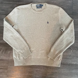 Grå stickad tröja från Polo Ralph Lauren - Säljer en klassisk grå stickad tröja från Polo Ralph Lauren i 100% bomull. Tröjan har rund halsringning, långa ärmar och den ikoniska lilla broderade loggan på bröstet. Bara att skriva om man har frågor kring plagget. Mvh FABIANFASHION 