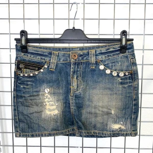 Minikjol i jeans med pärldetaljer - Lågmidjad minikjol i jeans med slitna detaljer och pärlor på fickorna. Kjolen har klassisk femficksdesign, knapp och dragkedja framtill. Strl: XS-S. Mått: Midja 78 cm, längd 28 cm.   /  Spara skärmtid, besök våra butiker i Sthlm, Malmö & Gbg. New arrivals daily + studentrabatt i alla våra butiker! Hitta till din närmsta butik på humansecondhand.se.   HUMANA Second Hand erbjuder 14 dagars retur, även via plick. Returer skickas med PostNord. Vid retur kontakta support@plick.se.