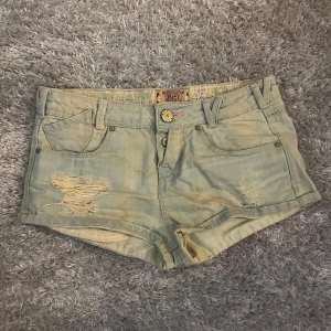 Ljusblå långmidjade jeansshorts från Bershka - Ett par lågmidjade Ljusblåa jeansshorts från Bershka med slitna detaljer och råa kanter. Perfekta för varma dagar och enkel att matcha med olika toppar.