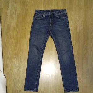 Mörkblåa Nudiejeans - Klassiska blå jeans med rak passform och fem fickor. Byxorna har normal midja och stängs med dragkedja och knapp. Perfekta för en avslappnad stil och passar till det mesta. Om ni har några frågor är det bara att höra av sig!
