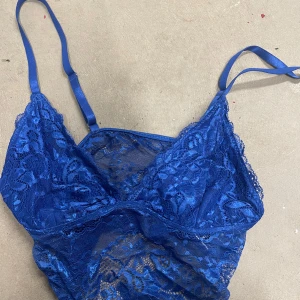 Blå spetsig linnetopp från SHEIN - Säljer en blå linnetopp från SHEIN med tunna axelband och vacker spetsdetalj. Toppen är genombruten med blommigt spetsmönster och har en feminin och trendig look. Perfekt för att skapa en snygg lager-på-lager-stil.