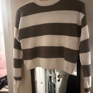 Randig stickad tröja från H&M - Säljer en stickad tröja från H&M med breda beige och vita ränder. Tröjan har rund halsringning och långa ärmar. Perfekt för en avslappnad och trendig look.