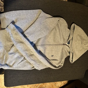 Grå hoodie med dragkedja från Polo Ralph Lauren - Säljer en klassisk grå hoodie från Polo Ralph Lauren med dragkedja och huva. Tröjan har två fickor framtill och en liten broderad logga på bröstet. Perfekt för en avslappnad och stilren look.!!!JAG HAR KVAR KVITTOT DET KOMMER MED KVITTOT!!!!