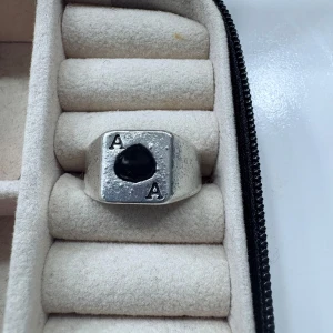 Silvrig ring med svart detalj och A-motiv - Cool ring i silverfärgad metall med en svart detalj i mitten och bokstaven A ingraverad på två sidor. Ringen har en chunky, fyrkantig design som sticker ut och passar perfekt för dig som gillar unika accessoarer.