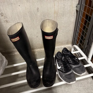 Svarta Hunter stövlar och svarta Nike sneakers - Säljer ett par klassiska svarta Hunter stövlar med högt skaft och ett par svarta Nike sneakers med vit sula och vit swoosh. Perfekta för regniga dagar och träning.