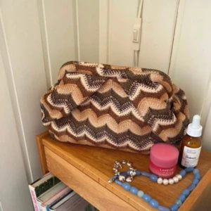 Mönstrad clutch i bruna toner - Säljer en snygg clutch med zigzag-mönster i beige, brunt och svart. Väskan har en unik form och stängs upptill. Invändigt finns ett fack med dragkedja. Helt ny och prislappen är kvar💖