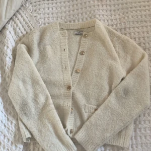 Vit kofta från Lindex  - Mysig vit kofta från Holly & Whyte by Lindex med dekorativa guldknappar och två fickor framtill. Denna koftan kommer inte längre till användning och hänger bara i min garderob, den har också två fläckar på armbågarna men inget som man lägger märke till. Orginal priset var 600 kr 🤍