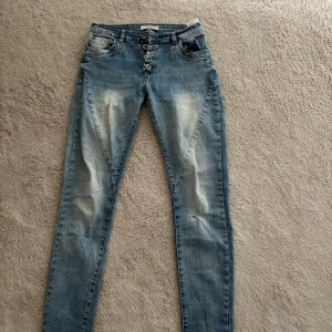 Blå jeansbyxor med knappar från Garment - Snygga blå jeansbyxor från Garment med flera knappar i gylfen och slitna detaljer framtill och baktill. Klassisk femficksmodell och normal passform. Perfekta till vardags för en avslappnad stil.
