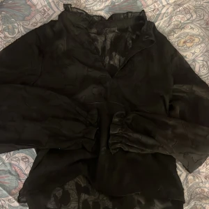 Svart blus - Svart feestblus, så classy å snygg!! Den har blomtyg som är lite genomskinligt med en v nacke, så fin till resturang å fina tillställningar. Ingen aning vart den är i från tyvärr men skulle gissa på vila, och att den är i S-M. 